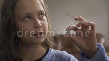 一个穿蓝色毛衣的生病的小女孩在检查绿色药丸。 在家接受治疗的白人儿童。